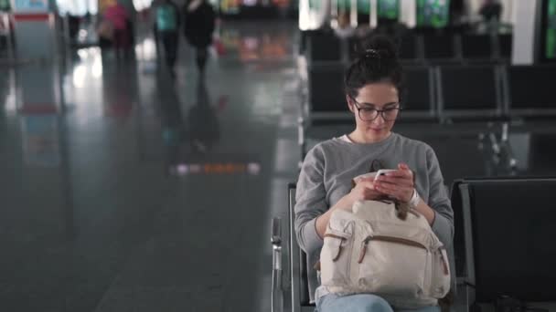 Chica utiliza teléfono inteligente en el salón del aeropuerto — Vídeos de Stock