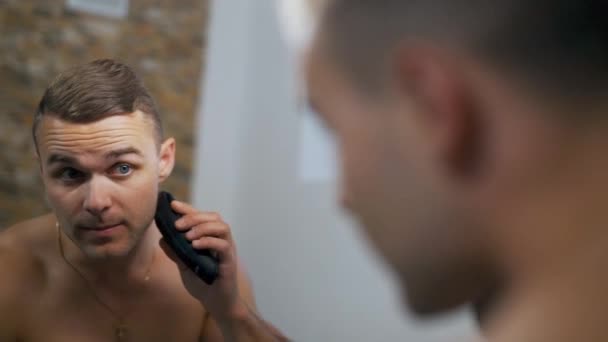 Chico se afeita y se mira en el espejo — Vídeo de stock