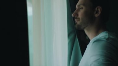 Adam perdeleri açar ve dışarı bakar.