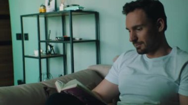 Adam evde otururken kitap okuyor.