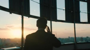 Üst düzey yönetici bir gökdelenin çatısında telefonla konuşuyor.