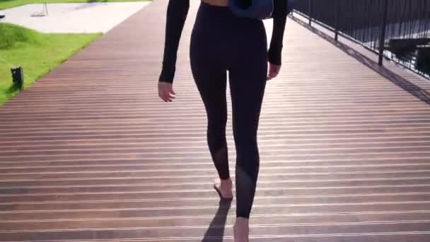 Ein Mädchen mit einer Fitnessmatte spaziert durch das Gelände des Business Centers — Stockvideo