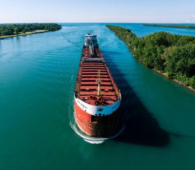 Mavi su yolunda ilerleyen büyük bir kargo gemisi.