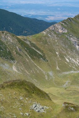 Açık mavi gökyüzünün altında yeşil dağlar ve vadiler