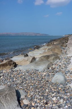 Çakıl taşları ve durgun mavi suyla kayalık kıyı şeridi