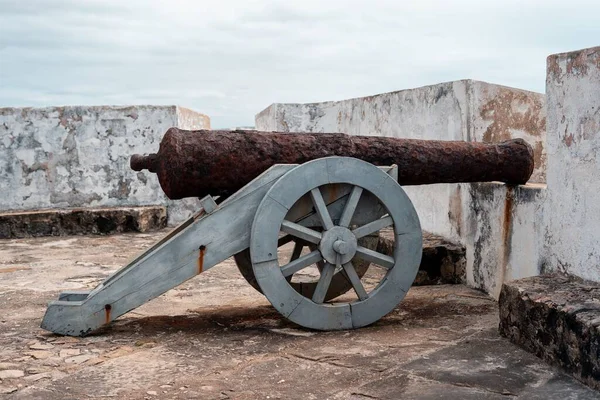 Bulutlu gökyüzüne ve uzak manzaraya bakan kale duvarına yerleştirilmiş eski bir top.