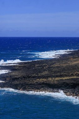 Kıyı manzaralı kayalık kıyı şeridi berrak gökyüzü altında mavi okyanus dalgaları çarpıyor.