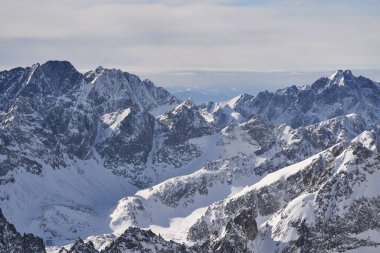 Karla kaplı dağ zirveleri gökyüzüne ulaşıyor, bulutlar engebeli arazide sürükleniyor..