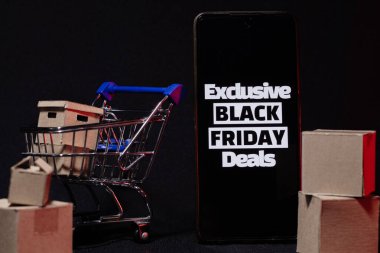 İçinde karton kutular ve cep telefonu olan mini market arabası, özel Kara Cuma Anlaşmaları metnini gösteriyor. Hızlı nakliye ve çevrimiçi perakende