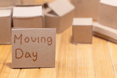 Tahtada el yazısıyla taşınma günü tabelası olan kutuları taşımak. Ev lojistiği ve nakliye