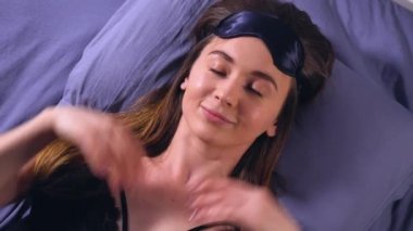 Kız yatakta uyuyor, uyanma veya uykuya dalmak. Yawns. Uyku maskesi için gözler giyiyor. Gülümsüyor ve kameraya doğru görünüyor. Poz