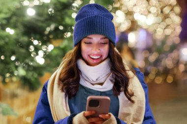 Şenlikli Noel festivali geçmişi olan, akıllı telefon kullanan mutlu bir kadın. İnternetten mesaj atıyor ya da Noel hediyesi sipariş ediyor.