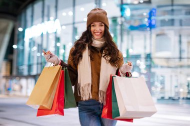 Akşamları alışveriş merkezinin önünde durup Noel hediyesi alan ve kış tatiline hazırlanan mutlu kadın portresi.