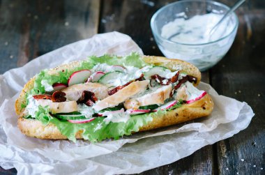 Sağlıklı tavuk sandviç ile tavuk, marul, turp, kurutulmuş domates, salatalık ve sos ahşap arka plan üzerinde Kapat.