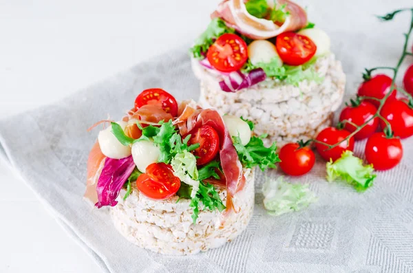 Healthy sandwich with rice cake, lettuce, mozzarella, cherry tomatoes and prosciutto