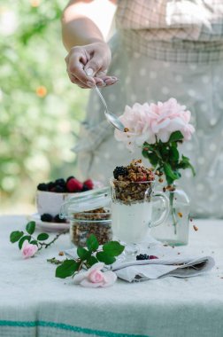 Kadının eller sağlıklı kahvaltı yediği gibi. Çilek ve granola masanın üzerine bir kase yoğurt.