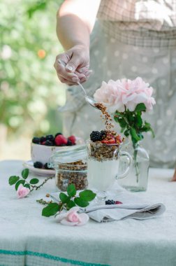 Kadının eller sağlıklı kahvaltı yediği gibi. Çilek ve granola masanın üzerine bir kase yoğurt.