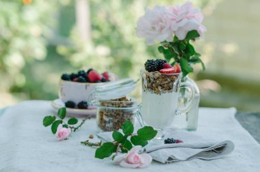 Kadının eller sağlıklı kahvaltı yediği gibi. Çilek ve granola masanın üzerine bir kase yoğurt.