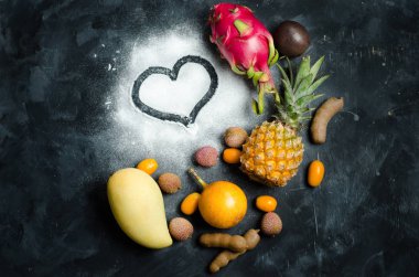 Kalp ve koyu arka plan üzerinde egzotik tropik meyveler. Ananas, mango, tutku meyve, demirhindi, granadilla, Kamkat, lychee, pitahaya, rambutan. Düz yatıyordu. Metin için yer