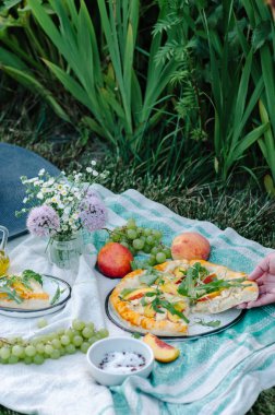 Tavuk, şeftali, krem peynir ve roka pizza. Pizza, üzüm, şeftali ve çiçekler ile çimlerde piknik