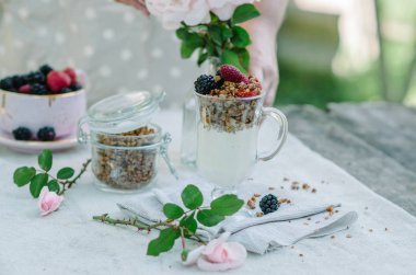 Kadının eller sağlıklı kahvaltı yediği gibi. Çilek ve granola masanın üzerine bir kase yoğurt.
