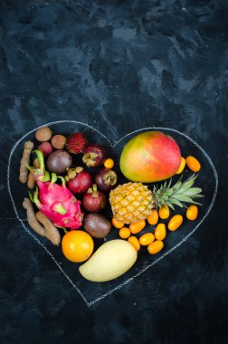 Koyu arka plan üzerinde egzotik tropik meyve yürekten. Ananas, mango, tutku meyve, demirhindi, granadilla, Kamkat, lychee, pitahaya, rambutan. Düz yatıyordu.
