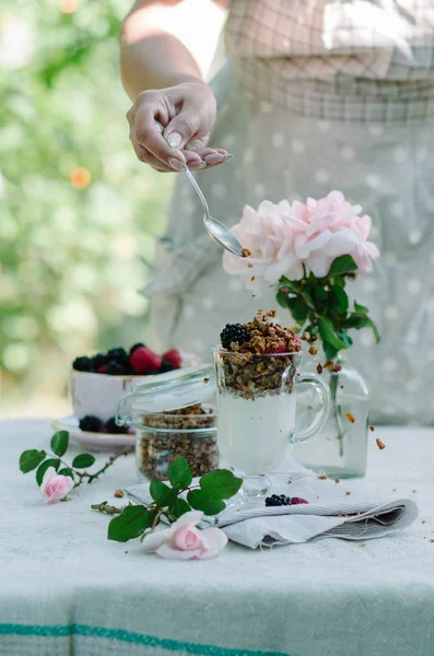 Kadının eller sağlıklı kahvaltı yediği gibi. Çilek ve granola masanın üzerine bir kase yoğurt.