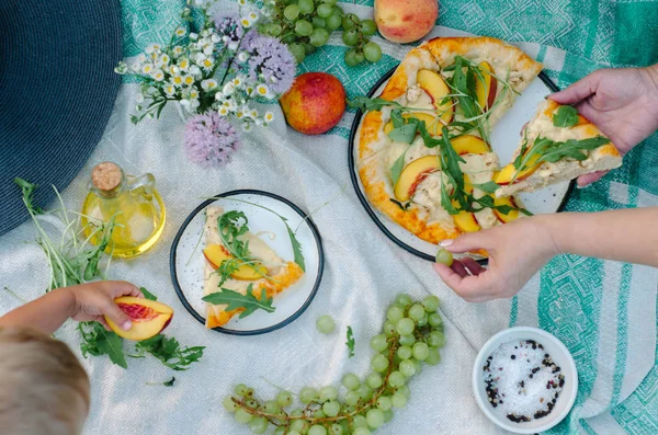 Pizza with chicken, peaches, cream cheese and arugula. Picnic on the grass with pizza, grapes, peaches and flowers