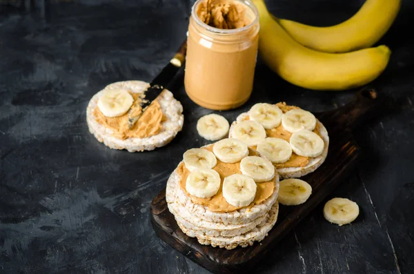 stock image Rice cakes with peanut butter and slices of banana on black wooden table. Space for text