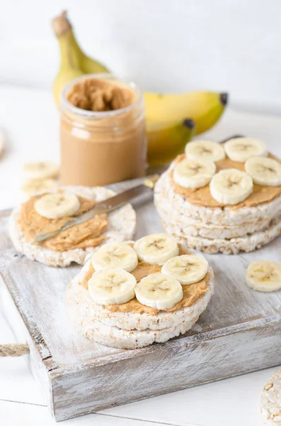 Healthy breakfast with rice cakes with peanut butter and slices of banana on white wooden table