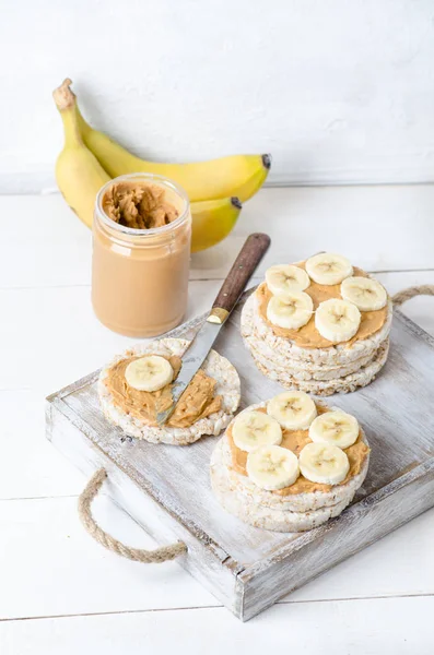 Healthy breakfast with rice cakes with peanut butter and slices of banana on white wooden table