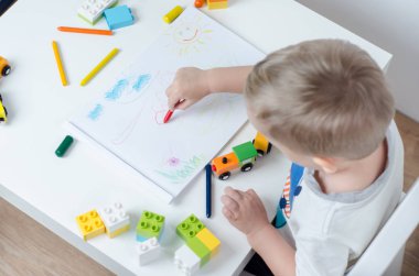 Küçük çocuk albümü içinde beyaz bir tablo çizer. Kalemler, tren, plastik bloğunda renkli çocuk odası.