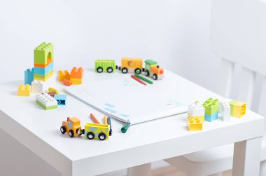 Beyaz masa kalem, oyuncak tren, renkli plastik blok ve çocuk çizimleri ile bir albüm ile parlak çocuk odasında. Çocuk çizim tablo.