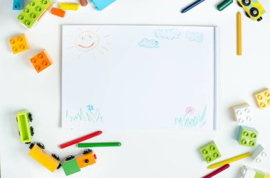 Üstten Görünüm kalemler, oyuncak tren, çok renkli plastik blok ve çocuk çizimleri ile bir albüm ile beyaz bir tablo. Düzen. Çocuk çizim tablo.