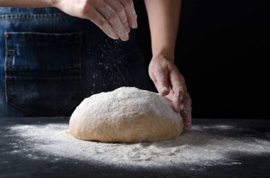 Koyu arka plan üzerinde taze hamur üzerine un yağmurlama eller.