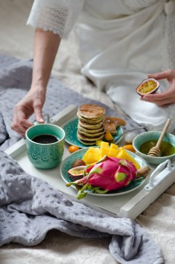 Tropikal meyve, krep ve kahve bir tepsi ile yatakta kahvaltı.