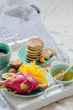 Tropikal meyve, krep ve kahve bir tepsi ile yatakta kahvaltı.