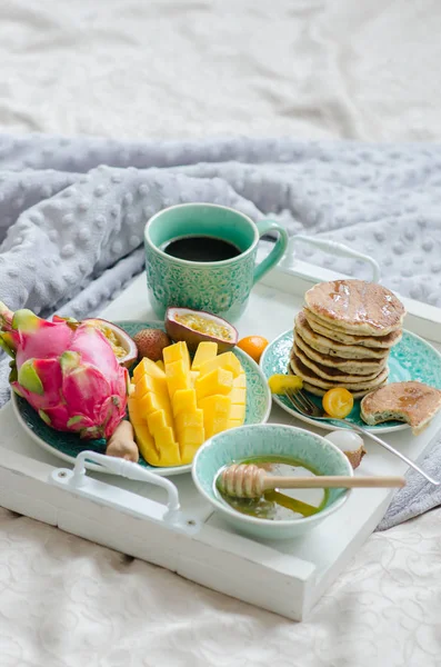 Tropikal meyve, krep ve kahve bir tepsi ile yatakta kahvaltı.