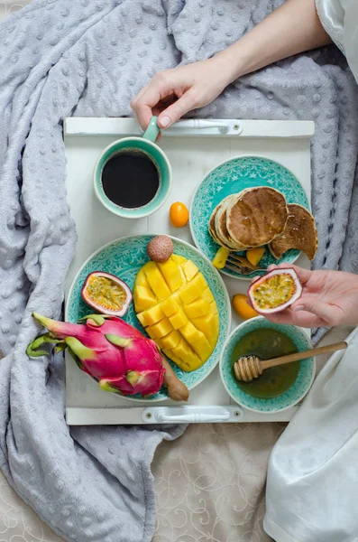 Breakfast in bed with tropical fruits, pancakes and coffee on a tray. — Stock Photo, Image