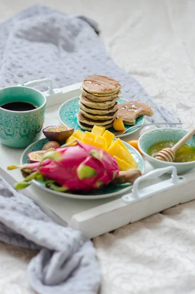 Café da manhã na cama com frutas tropicais, panquecas e café em uma bandeja . — Fotografia de Stock