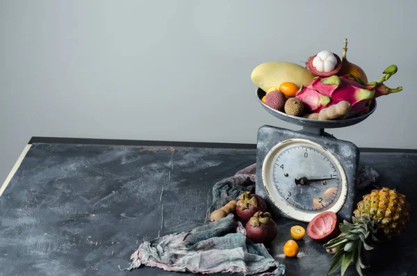 Tropical fruit on vintage scales on black background. — Stock Photo, Image