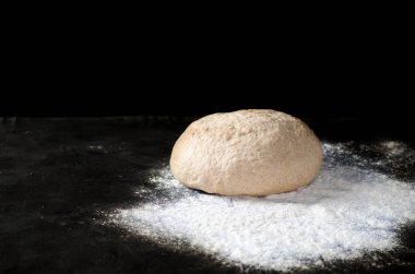 Siyah bir zemin üzerine dökülmüş un ile hamur. Ekmek, rulo, pizza, elmalı veya pasta hamur mayaları. Sağlıklı ekmek üzerinden kepekli un yemek. Kopya alanı.