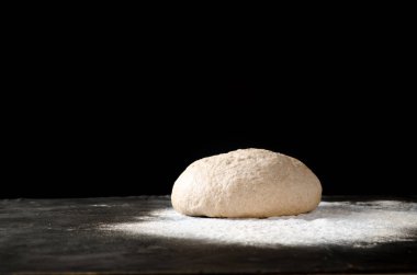 Siyah bir zemin üzerine dökülmüş un ile hamur. Ekmek, rulo, pizza, elmalı veya pasta hamur mayaları. Sağlıklı ekmek üzerinden kepekli un yemek. Kopya alanı.