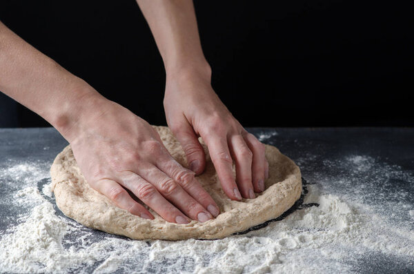 Hands knead the dough for pizza making.