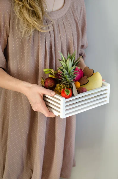Fruit creative serving. Woman\'s hands holding a wooden box with exotic fruits. Romantic gift. Passion fruit, strawberries, pitahaya, lychee, mango