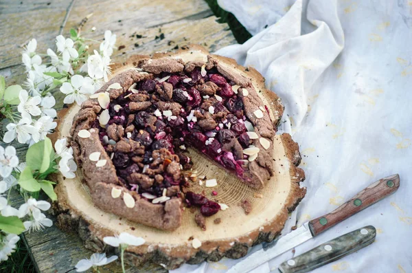 Galette de cereja de chocolate ou torta em uma tábua de madeira. Piquenique de primavera ou verão na natureza . — Fotografia de Stock