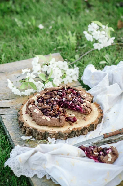 Galette de cereja de chocolate ou torta em uma tábua de madeira. Piquenique de primavera ou verão na natureza . — Fotografia de Stock