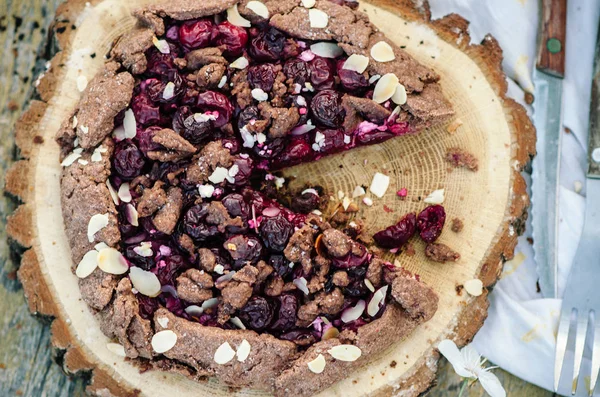 Schokoladen-Kirsch-Galette oder Kuchen auf einem Holzbrett. Frühjahrs- oder Sommerpicknick in der Natur. — Stockfoto