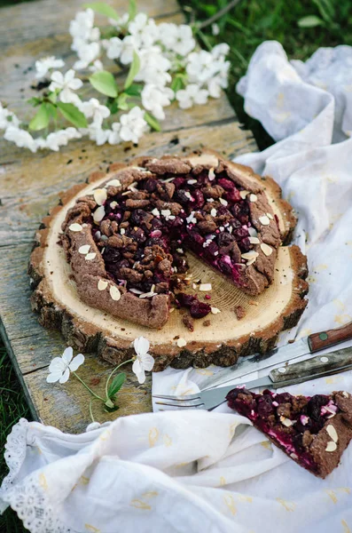 Schokoladen-Kirsch-Galette oder Kuchen auf einem Holzbrett. Frühjahrs- oder Sommerpicknick in der Natur. — Stockfoto