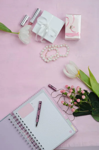 Women's accessories in white and pink colors, flowers, notebook with pen, cosmetics and gift boxes. Beauty women flat lay. Top view.